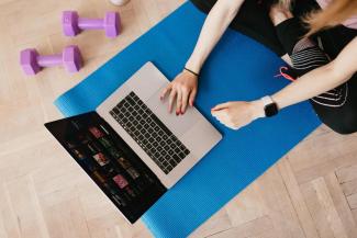 Donna che lavora al computer sopra un tappetino da yoga con due piccoli pesi vicino